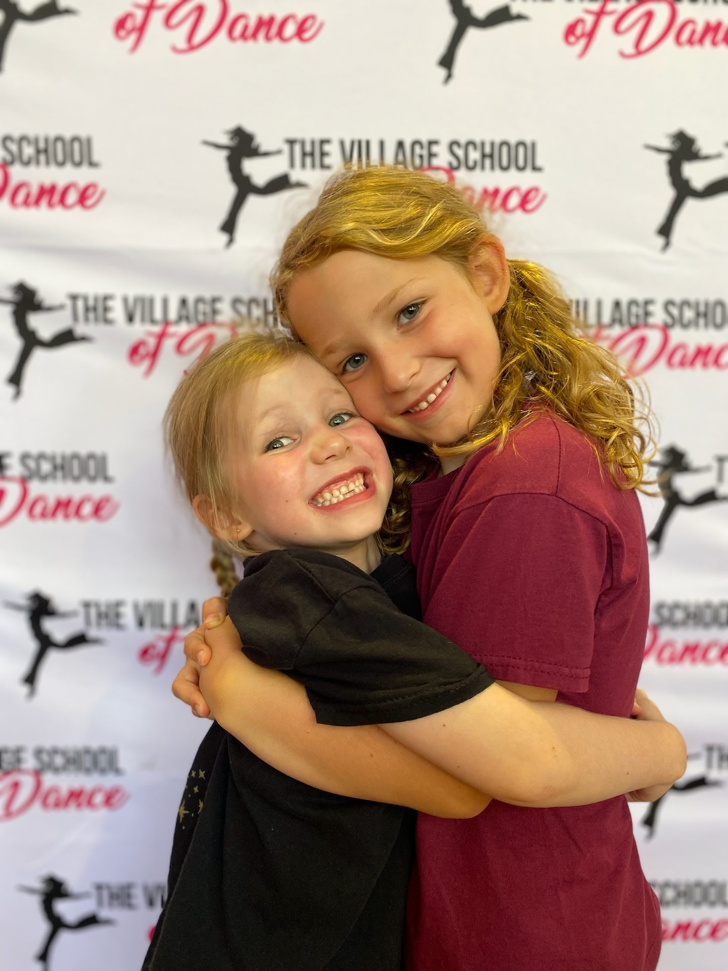 Two dancers hugging in front of The Village School of Dance backdrop